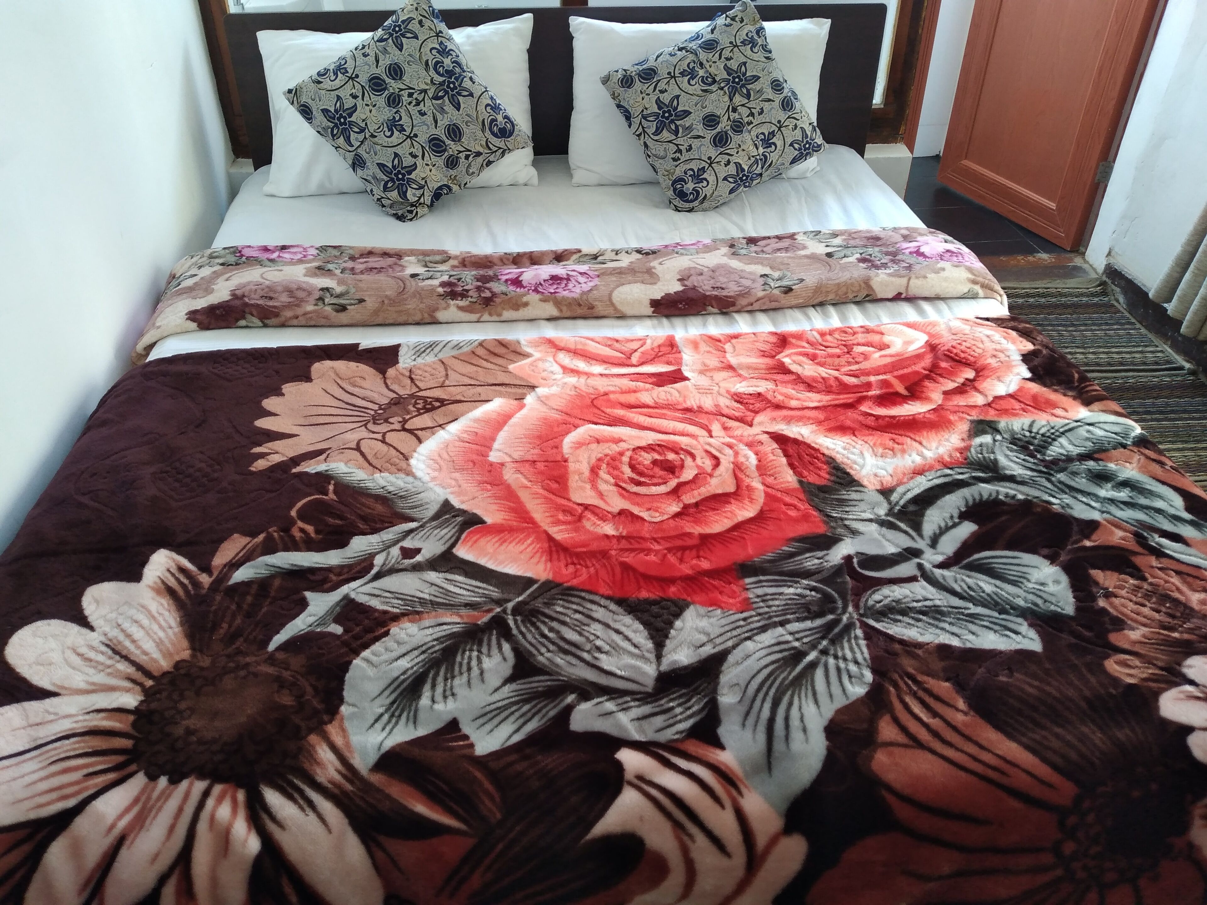 Una cama con colcha estampada, dos almohadas decoradas y cabecera de madera.