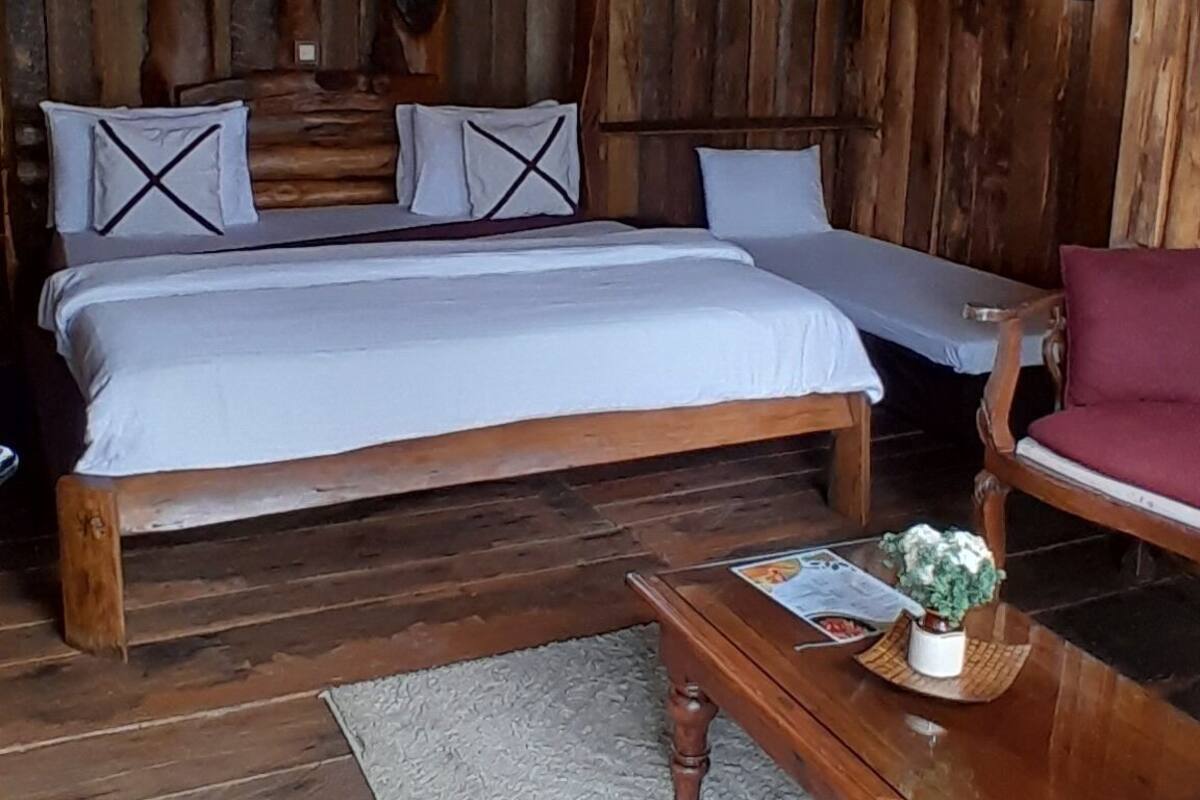 Une chambre rustique aménagée dans un chalet en bois, avec un grand lit, un banc en bois et une petite table agrémentée d’une plante.