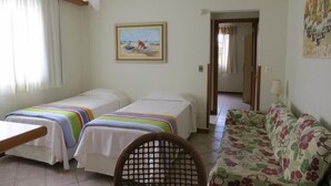 Una habitació amb dos llits, un sofà, una cadira, un ventilador de sostre i un quadre a la paret.