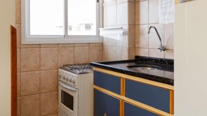 Una cuina amb fogó de gas, un rentaplat i una finestra.
