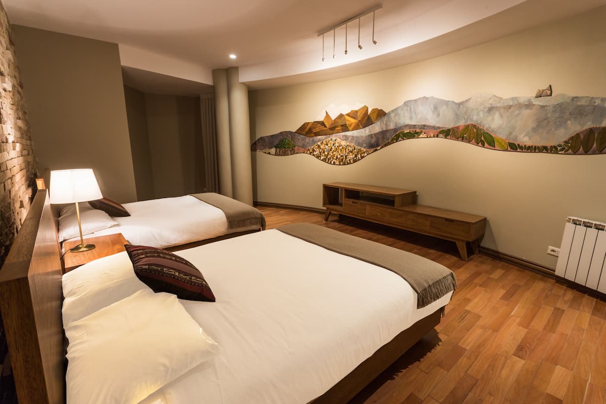 Una habitación de hotel con dos camas, un banco de madera, un mural en la pared y un radiador.