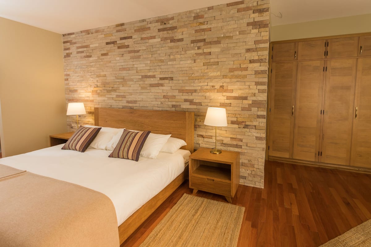 Un dormitorio con una cama de madera, dos mesitas de noche con lámparas, una pared con diseño de ladrillo y armarios de madera.
