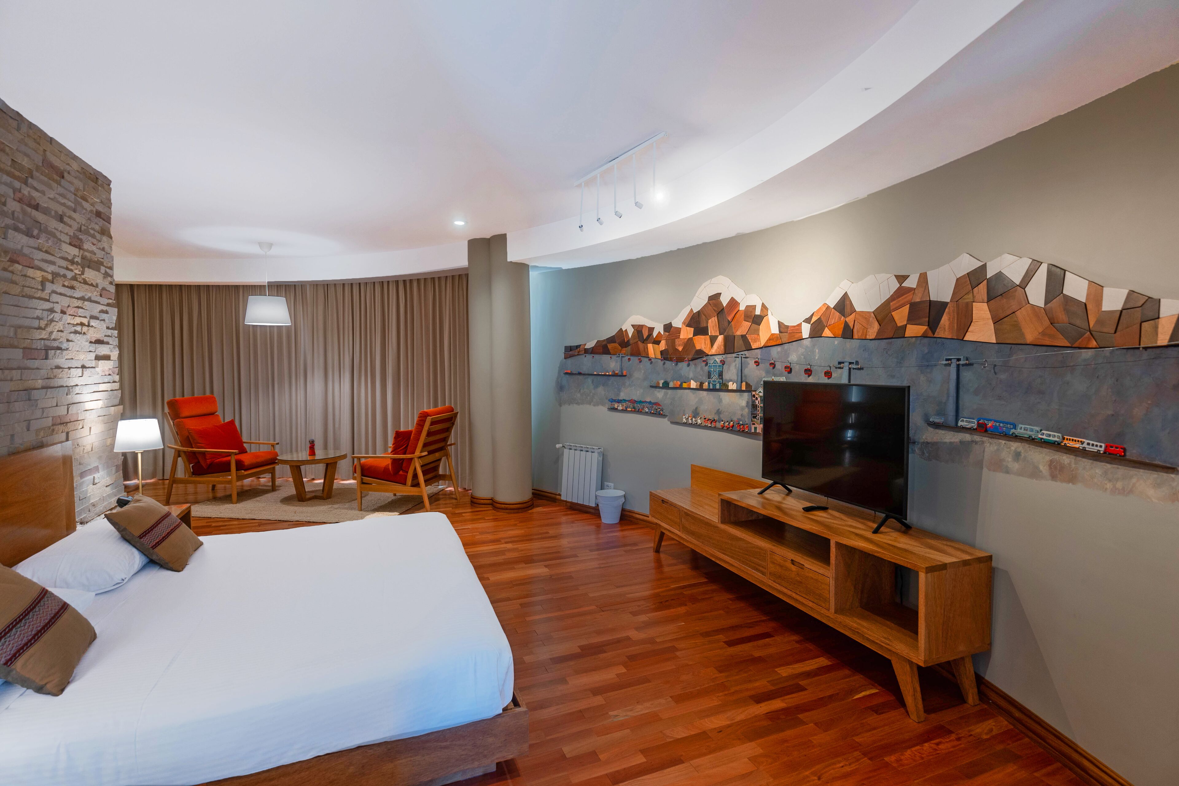 A hotel room with a large bed, a TV, a wooden bench, and a wall-mounted TV shelf.