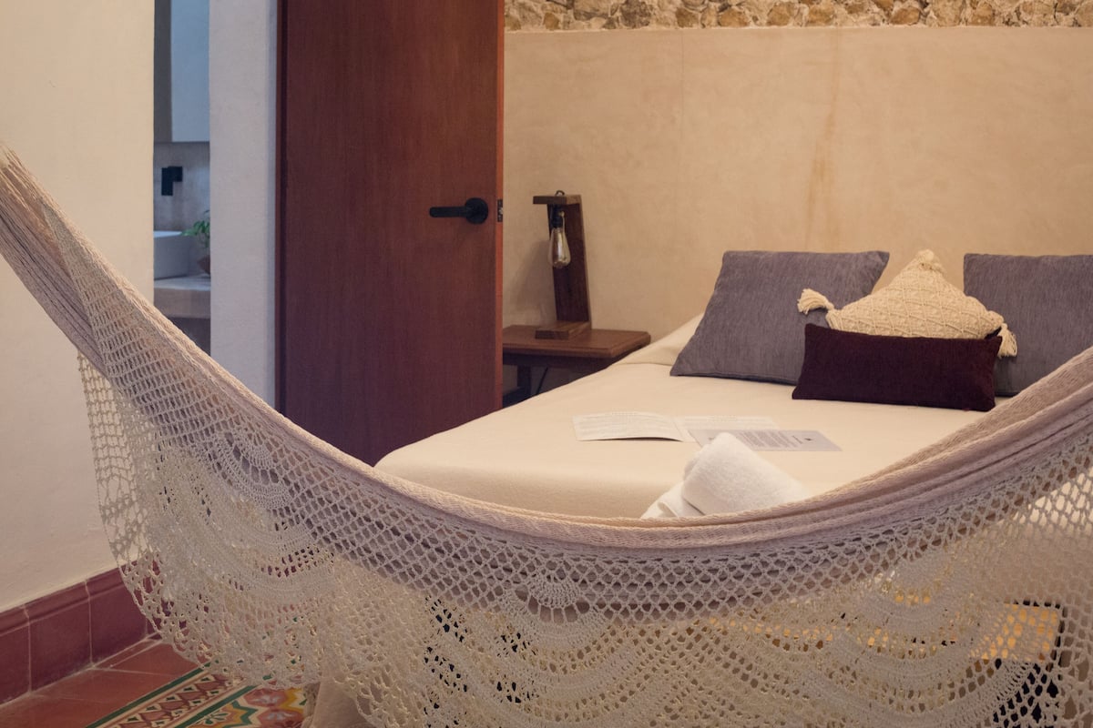 A hammock in a room with a bed, a nightstand, and a door.