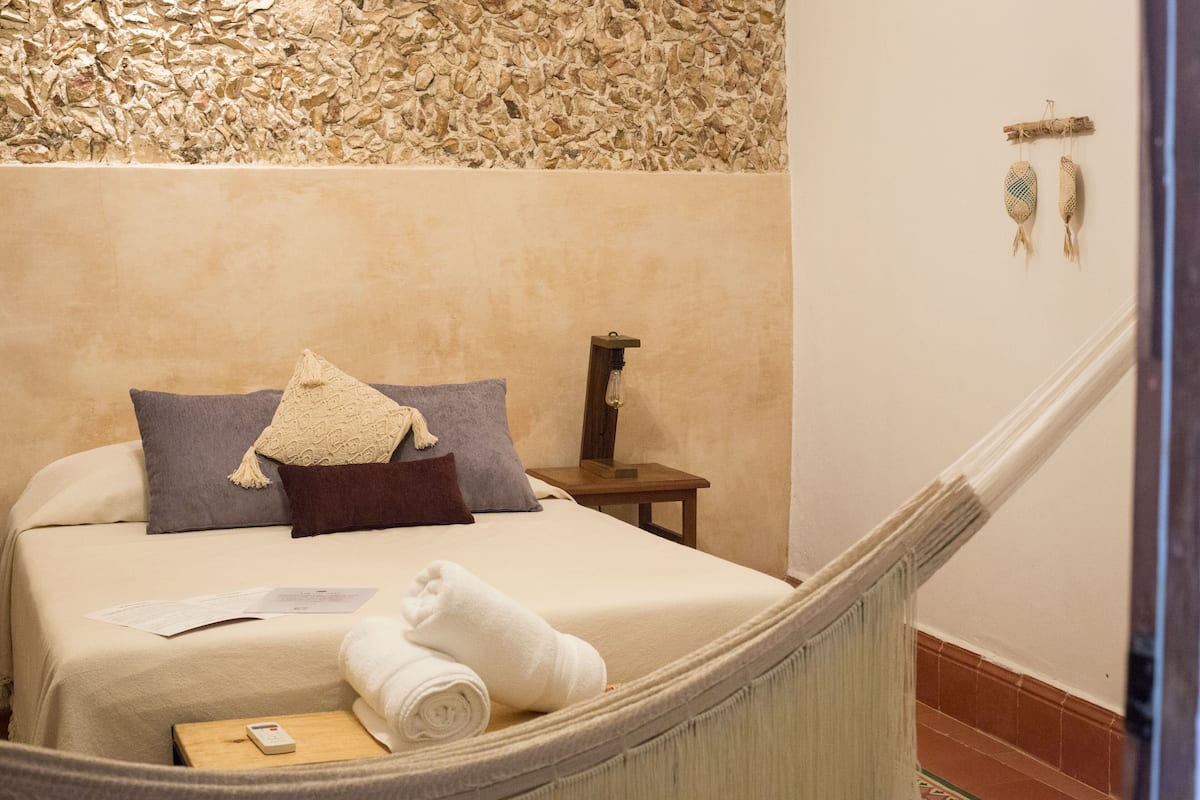 A neatly made bed with a pillow, a bedside table with a lamp, and a hammock.