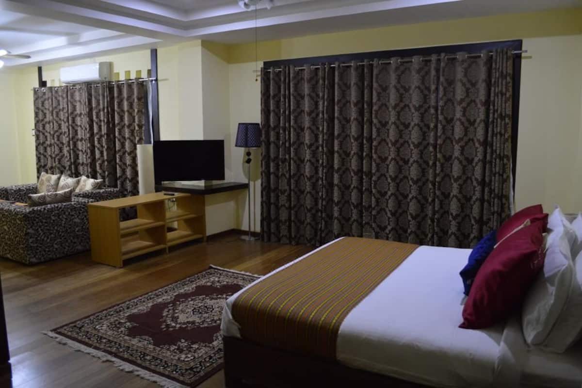 Una habitación de hotel con cama, televisión, sofá y cortinas.