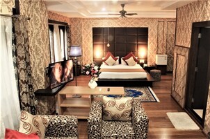 A hotel room with a large bed, a television, a desk, and patterned furniture.
