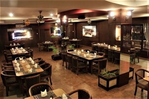 A restaurant with multiple dining tables and chairs, ceiling fans, and wall-mounted televisions.