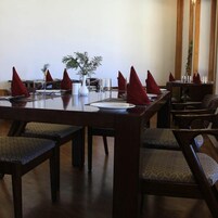 Un comedor con una mesa larga dispuesta para varios comensales, sillas de madera con cojines estampados y un florero con follaje sobre la mesa.