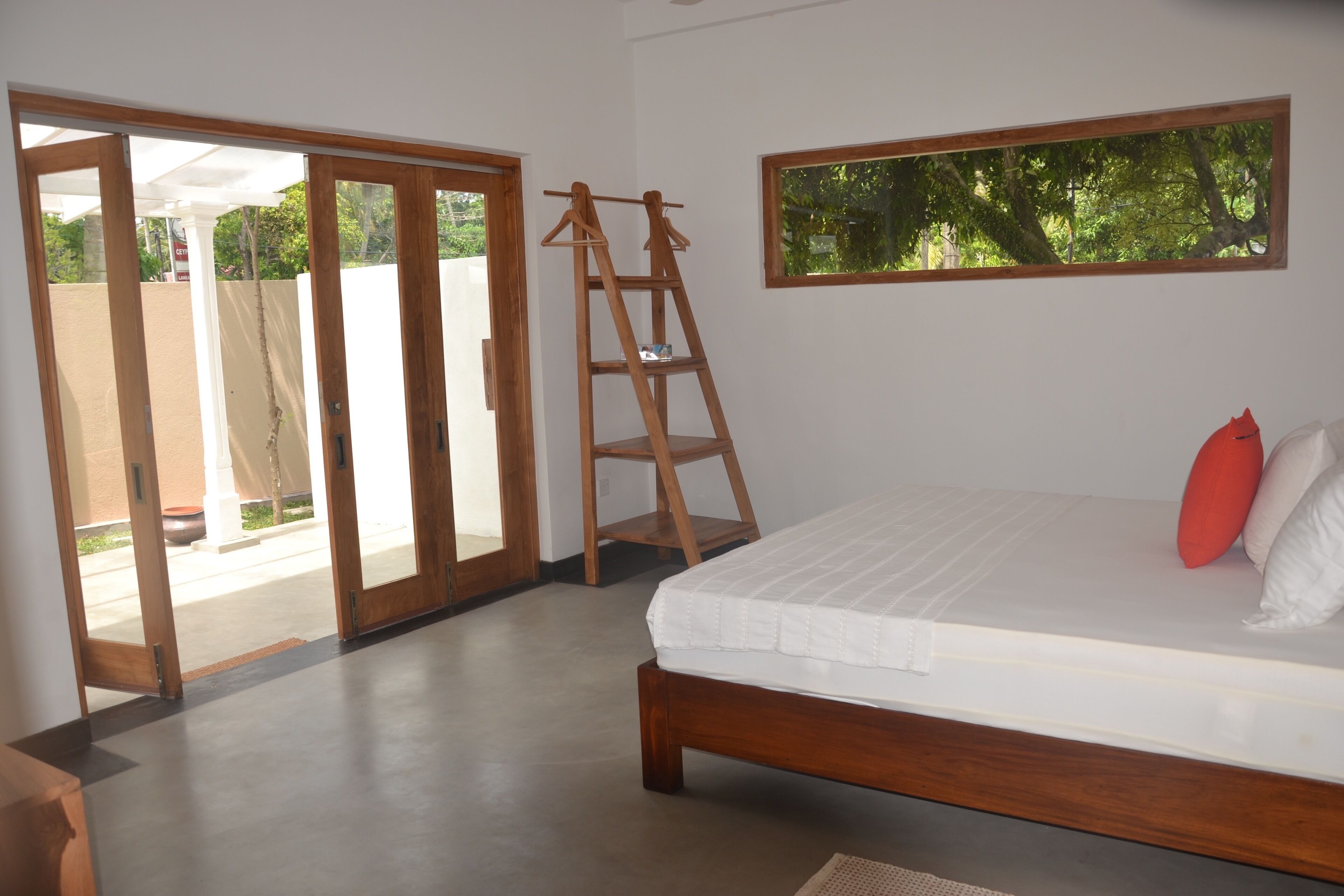 A bedroom with a wooden bed, a ladder, a window with a view of trees, and a sliding glass door leading to an outdoor area.