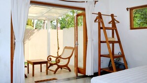 Una habitación con una cama, una silla de madera, una mesita pequeña, una escalera y una puerta corrediza de vidrio que da a un espacio al aire libre.