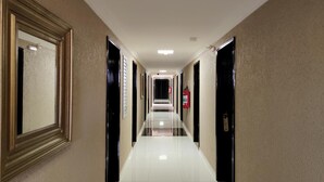Un couloir d’hôtel avec un mur recouvert de miroirs, des portes noires et un extincteur.