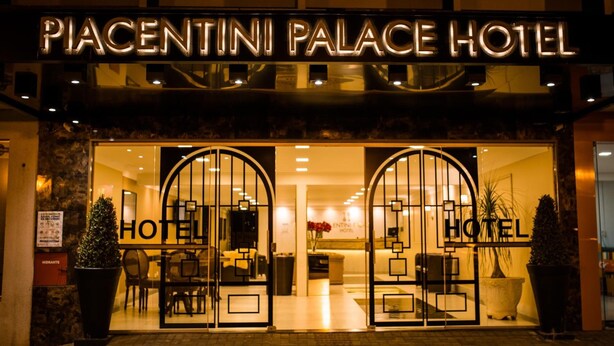 L’entrée de l’hôtel Piacentini Palace, avec sa façade en verre, un espace d’accueil et deux grands plantes en pot.