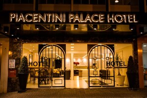 The entrance of the Piacentini Palace Hotel with a glass facade, a reception area, and two large potted plants. - Piacentini Palace Hotel (Campo Mourao)