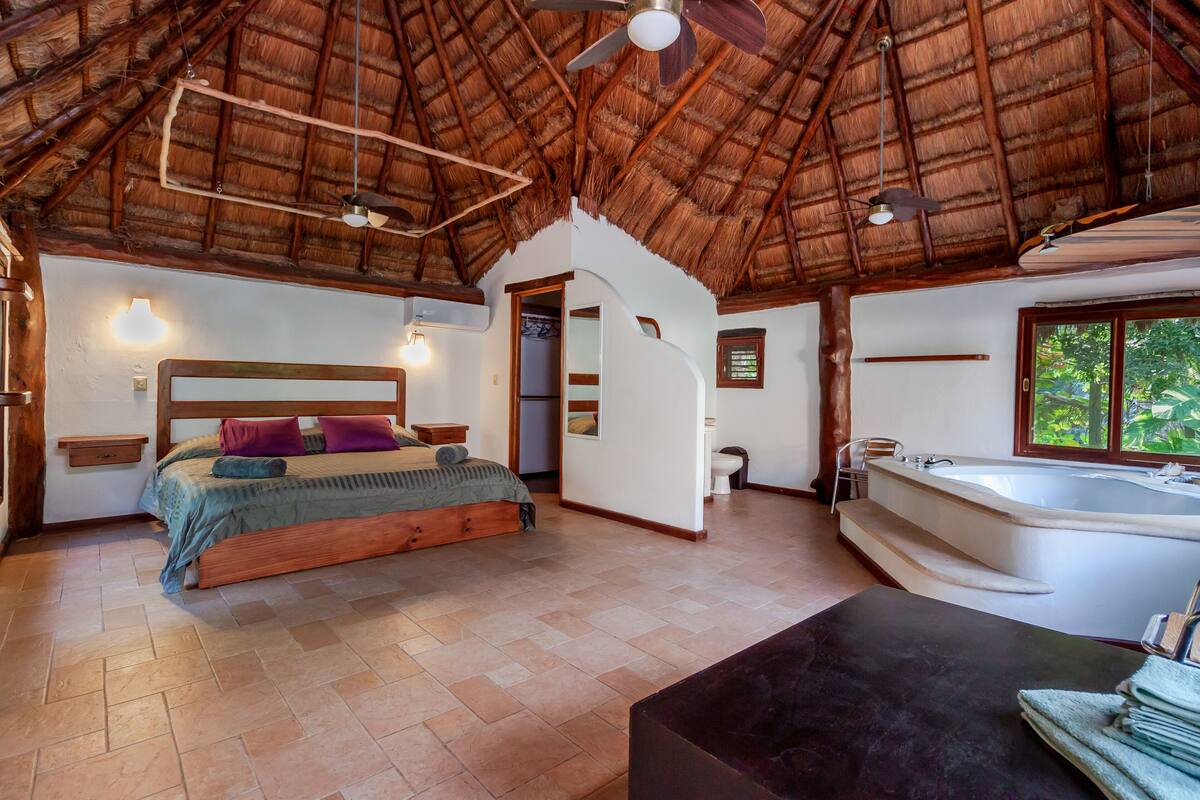 Quarto com cama de madeira, um banco embutido, banheira e ventoinha no teto.