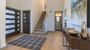 Una escalera que lleva al segundo piso, una puerta de madera oscura, una alfombra y un cuenco decorativo sobre una consola de madera.