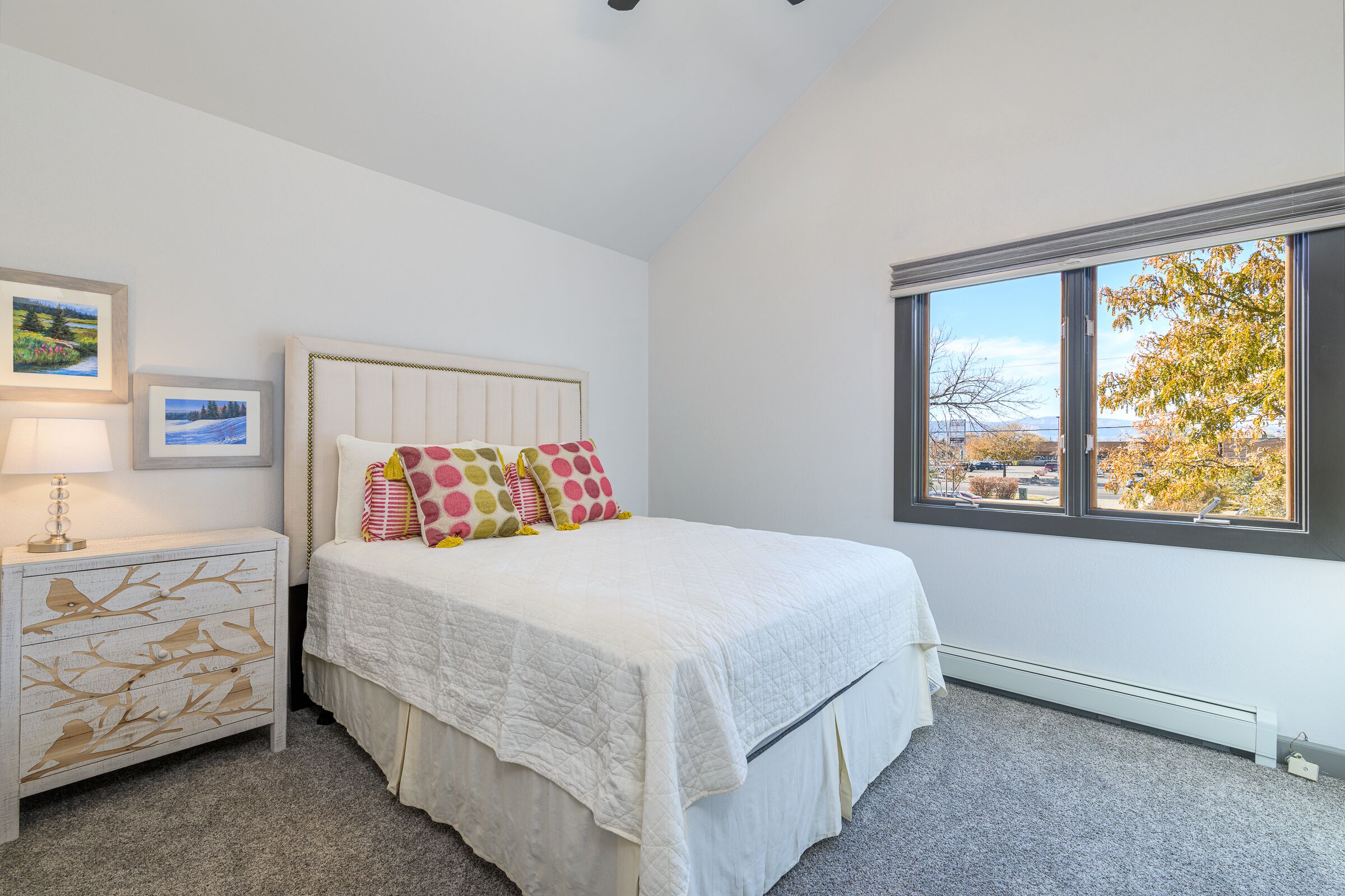A bedroom with a bed, a nightstand, a dresser, and a window with a view of trees.