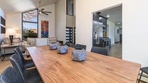 Amplia sala de estar con una gran mesa de comedor de madera, asientos cómodos, un ventilador de techo y vista a la cocina.