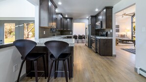 Una cocina moderna con armarios de madera oscura, una isla grande con taburetes de bar y vistas al área de estar.