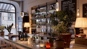 A bar area with shelves of wine bottles, a menu board, and potted plants. - Villa Dagmar (Stockholm)