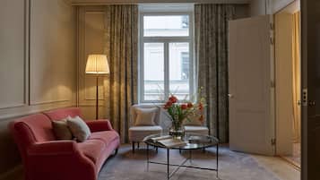 A living room with a red sofa, a white armchair, a glass coffee table with a book and flowers, and a lamp.