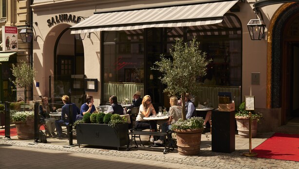 An outdoor cafe with tables and chairs, potted plants, and a red carpet leading to the entrance. - Villa Dagmar (Stockholm)