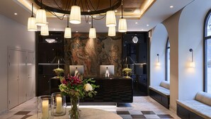 A reception area with a checkered floor, a round table with candles and flowers, and a wall with a mural. - Villa Dagmar (Stockholm)