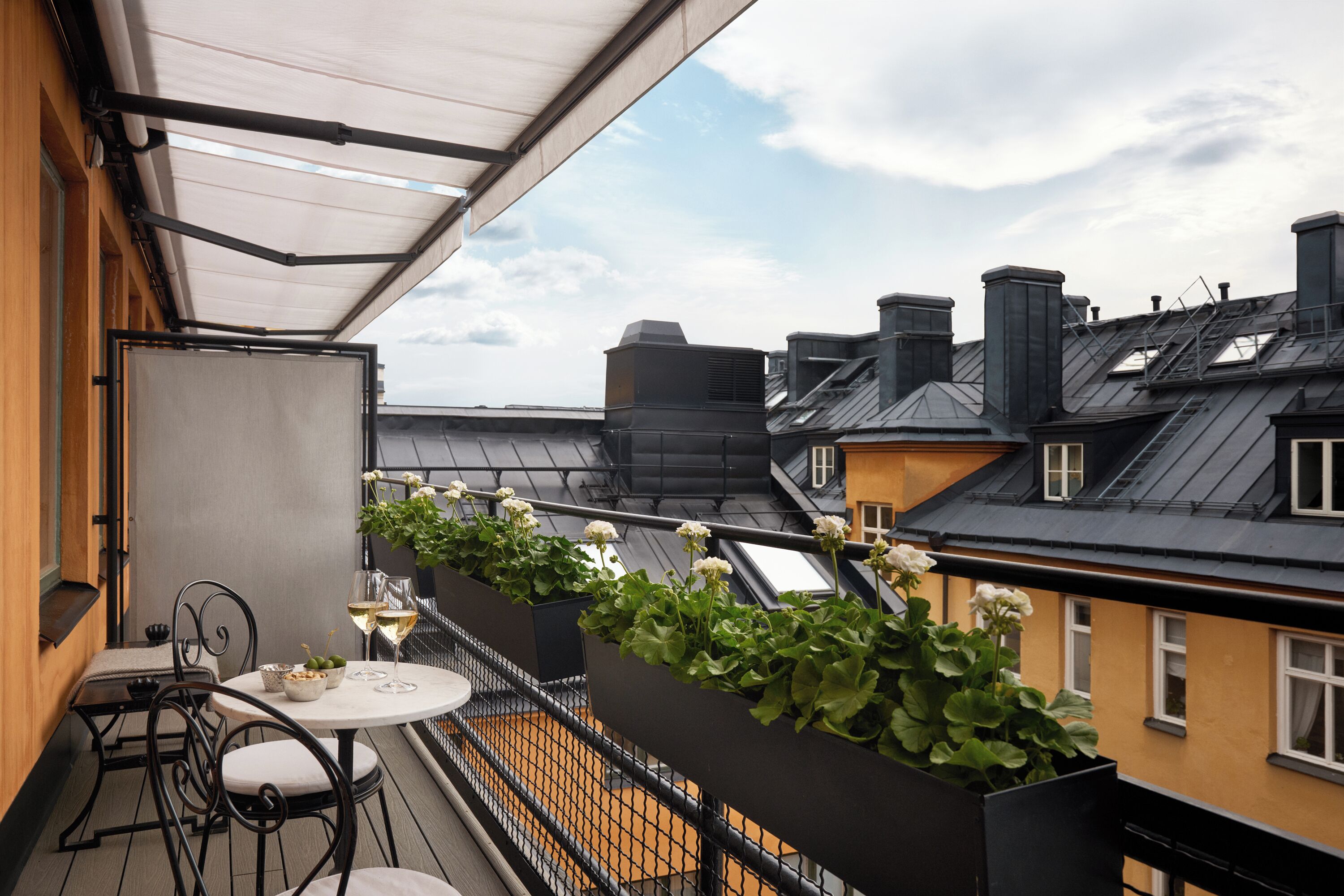 A balcony with a table, chairs, and potted plants.