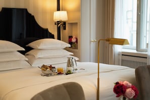 A hotel room with a neatly made bed, a bedside table with a lamp, a window with curtains, and a view of the outside. - Villa Dagmar (Stockholm)