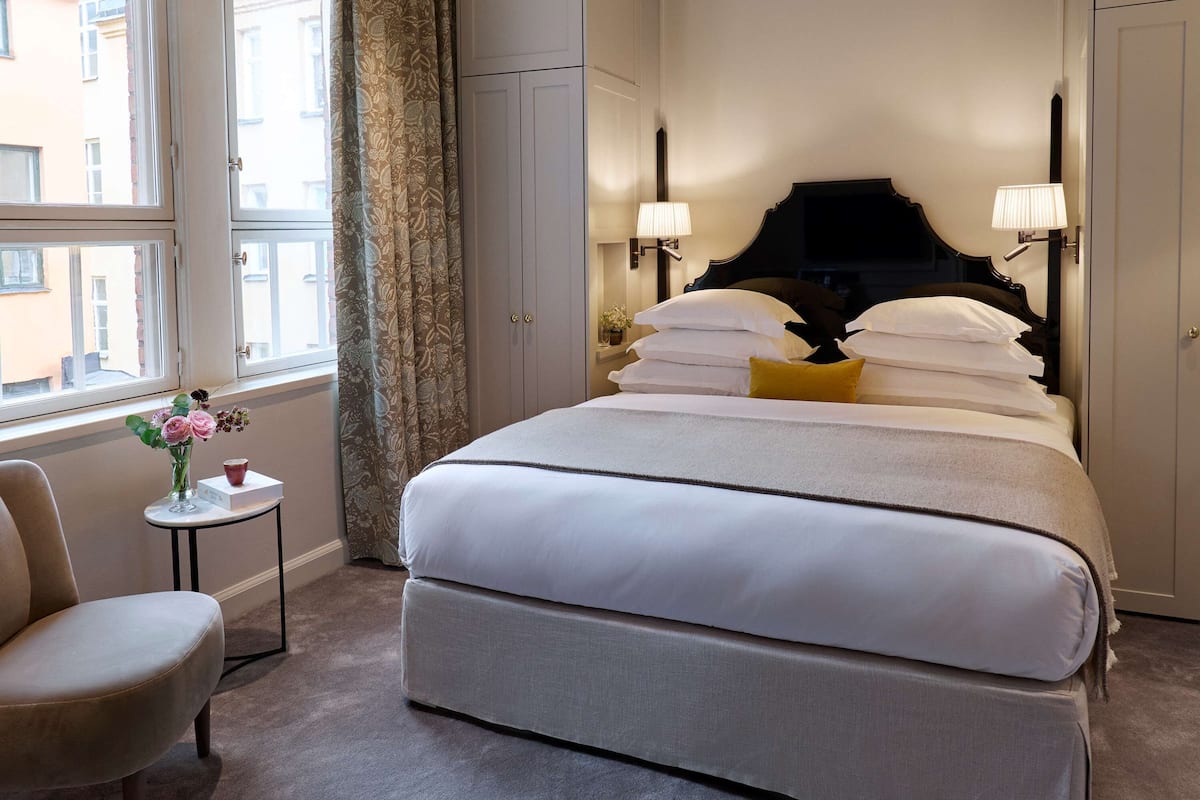 A neatly arranged hotel room with a large bed, bedside lamps, a small table with a vase of flowers, and a chair.