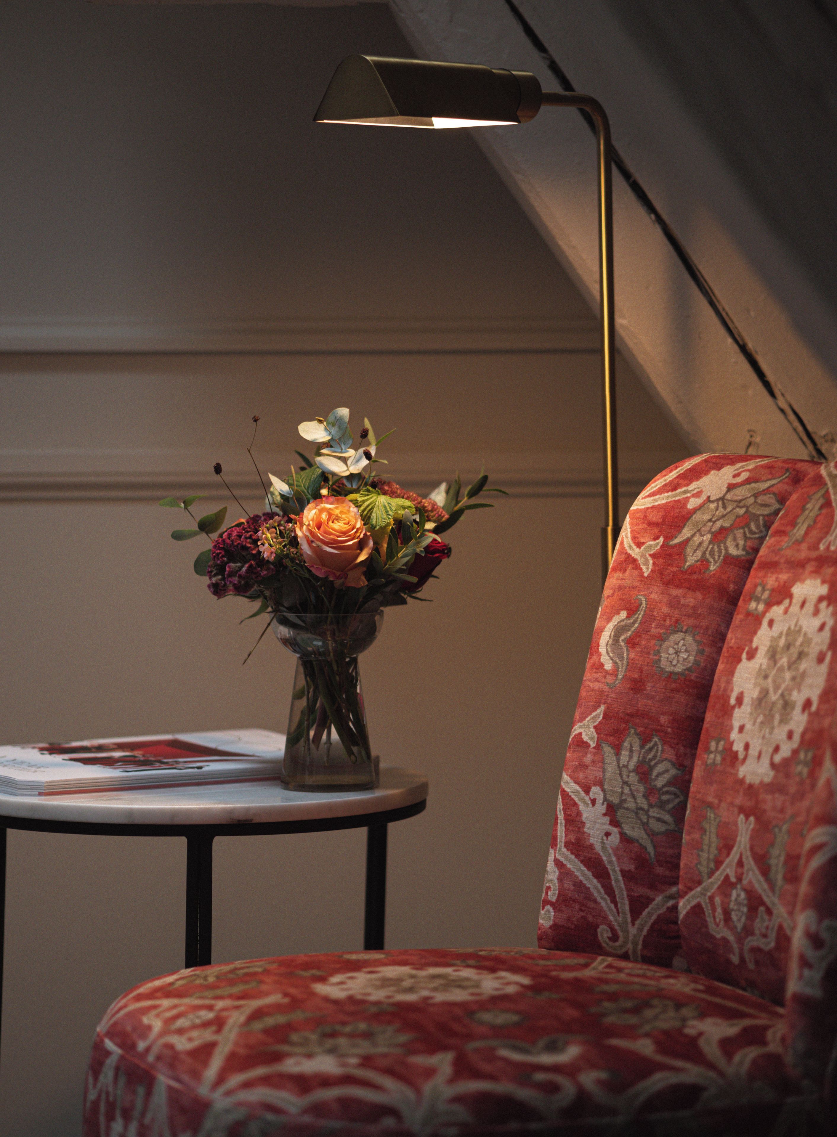 Una habitación con un sofá rojo estampado, una pequeña mesa redonda con un florero y una lámpara de pie alta.