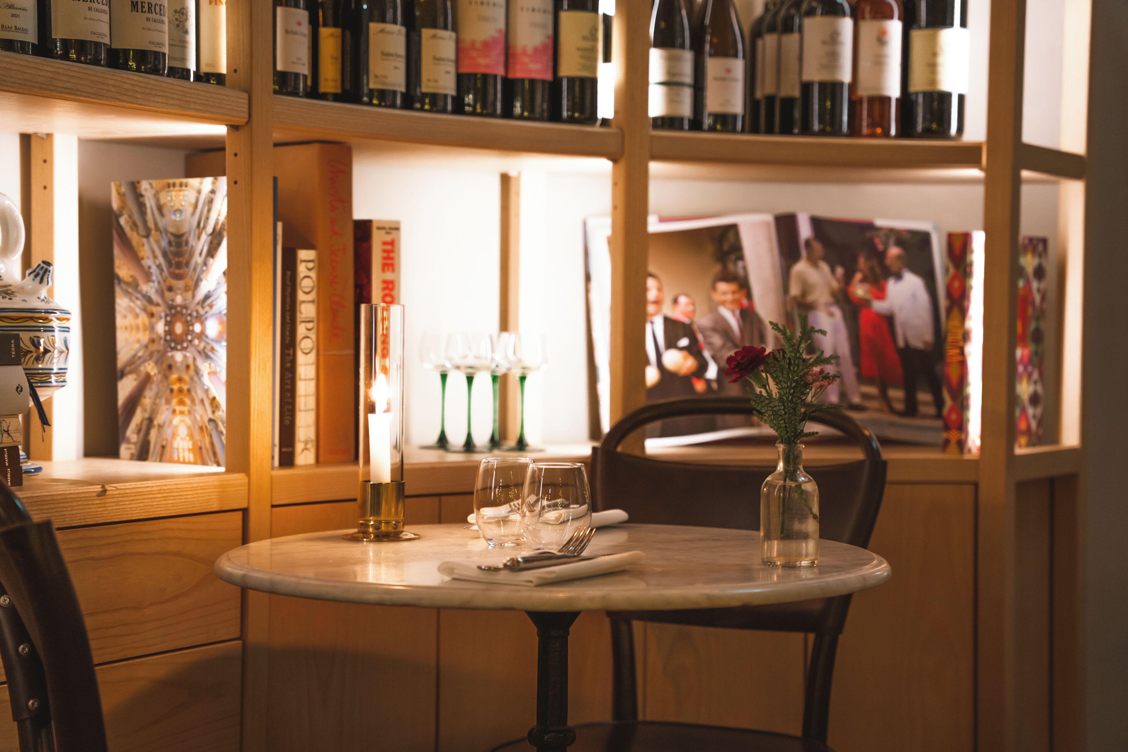 Interior de restaurante con una mesa redonda lista para comer, botellas de vino en estanterías y cuadros en la pared.