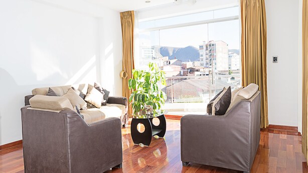 A modern living room with two grey sofas, a glass coffee table, and a large window with a view of buildings and mountains. - Parque 5 Apart Hotel (Cusco)