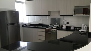 A modern kitchen with a black countertop, stainless steel appliances, and white cabinetry. - Parque 5 Apart Hotel (Cusco)