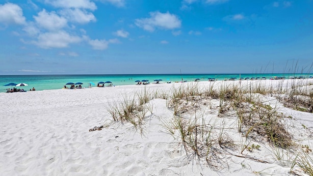Ein Strand mit weißem Sand, klarem türkisblauem Wasser und einigen Sonnenschirmen.