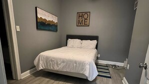 A bedroom with a bed, a ceiling fan, a painting, and a 'HOME' sign on the wall. - No Place Like a Home Away From Home (New Orleans)