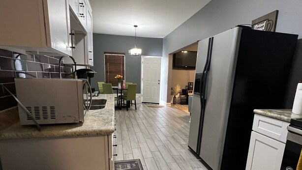 A modern kitchen with a refrigerator, microwave, and stove. There is a dining area with a table and chairs. - No Place Like a Home Away From Home (New Orleans)