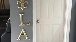 A door with a white frame and a grey wall with decorative gold letters spelling "NOLA" and a fleur-de-lis symbol. - No Place Like a Home Away From Home (New Orleans)