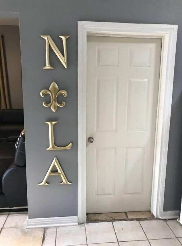 Een deur met een witte omlijsting en een grijze muur met decoratieve gouden letters die 'NOLA' spellen en een toekan symbool.