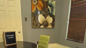 A dining area with a round table, a green upholstered chair, and a floral artwork on the wall. - No Place Like a Home Away From Home (New Orleans)