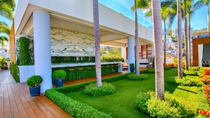 A modern outdoor area with a wooden deck, a seating area with chairs, and a well-maintained garden with various plants and flowers. - Pier 57 Stunning Ocean View Corner Unit w/ Balcony (Emiliano Zapata)