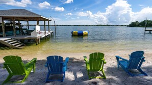 Een strand met groene en blauwe Adirondack-stoelen, een overdekte steiger en een drijvend platform.