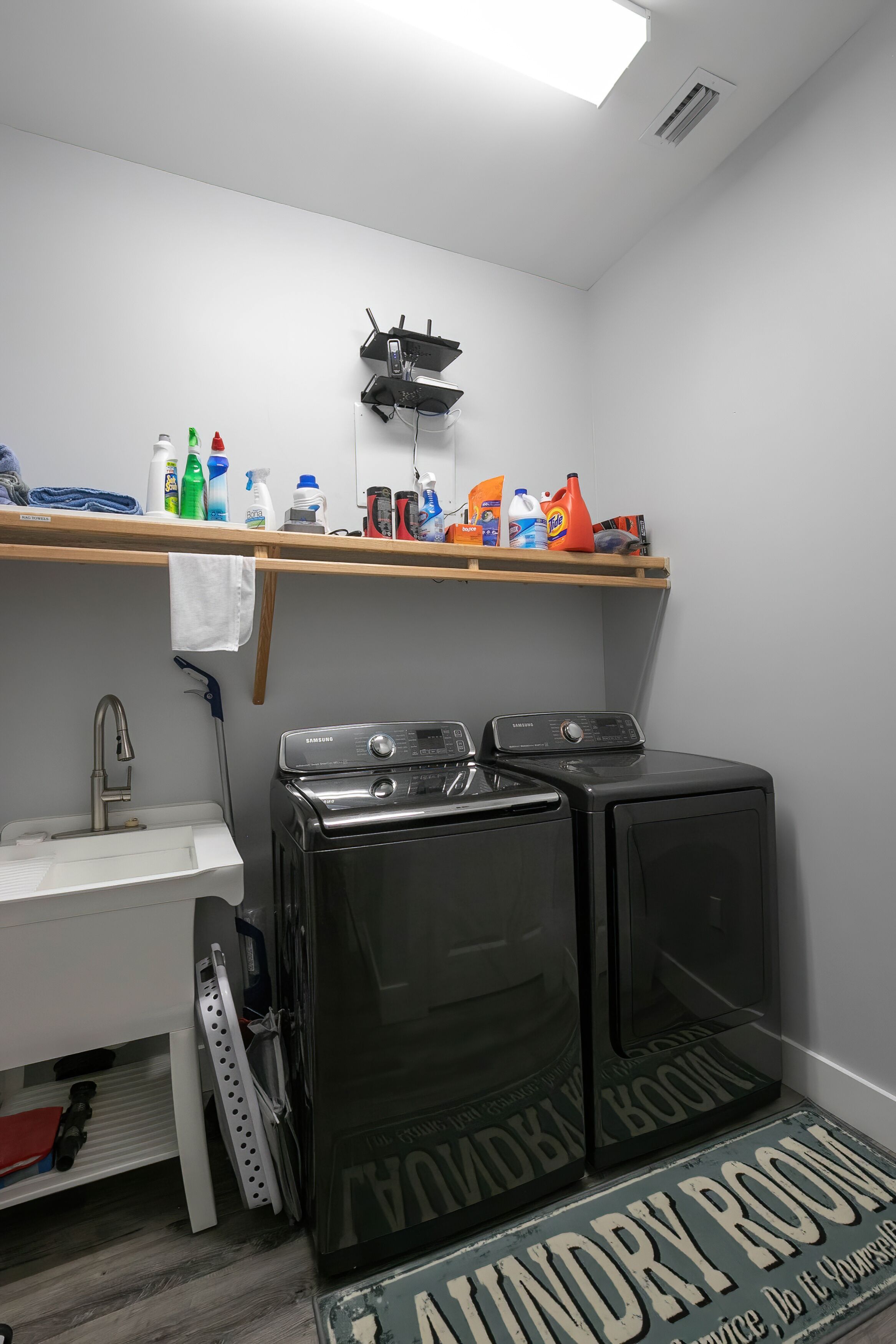 Una lavandería con dos lavadoras negras, un lavabo y un estante con productos de limpieza.