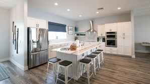 Een moderne keuken met een groot eiland, roestvrijstalen apparatuur, witte kastjes en een backsplash met een herringbone-patroon.