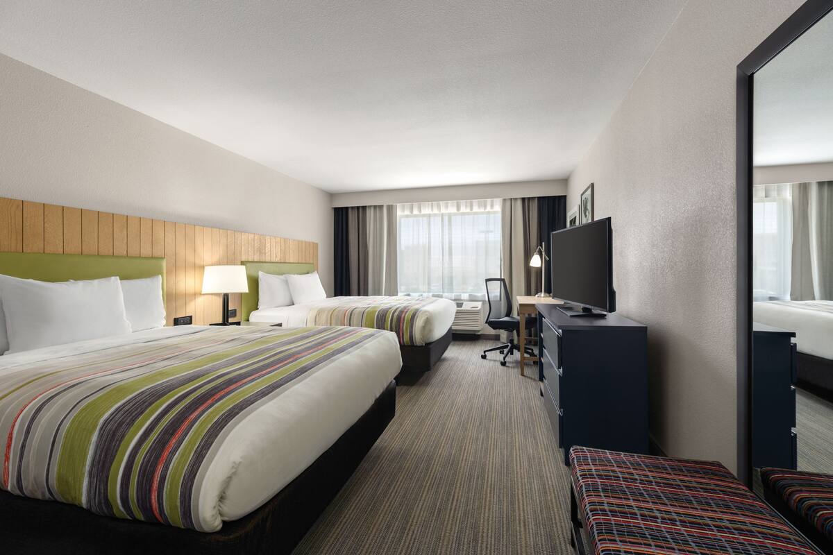 A hotel room with two beds, a desk, a television, and a large mirror.