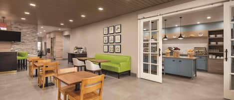 A modern interior with wooden tables and chairs, a green sofa, and a kitchen area with blue cabinets.