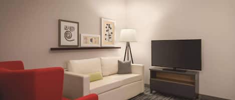 A hotel room with a white sofa, red armchair, and a flat-screen TV on a stand.