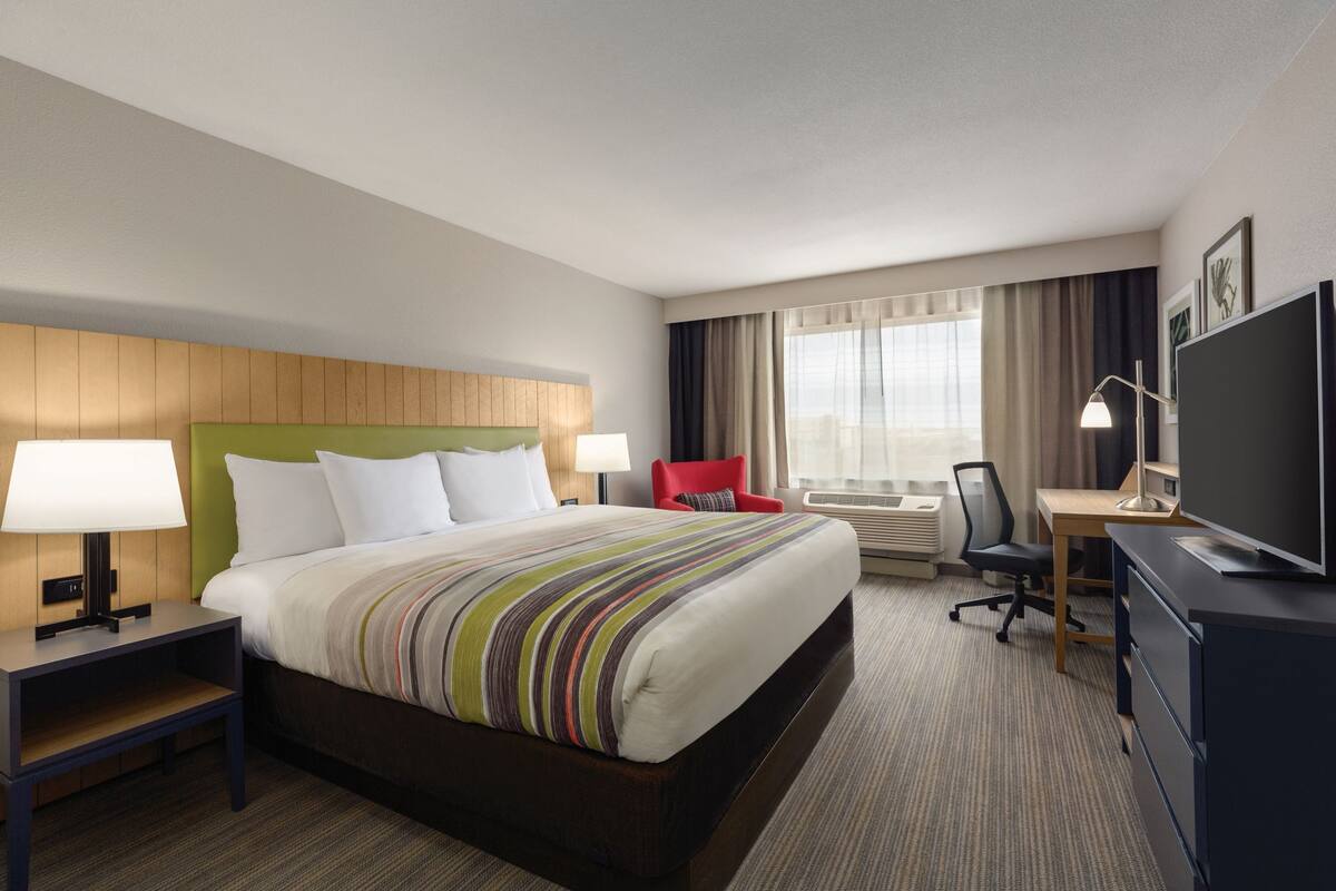 A hotel room with a large bed, a desk, a TV, and a chair.