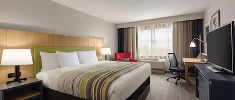 A hotel room with a large bed, a desk, a TV, and a chair.