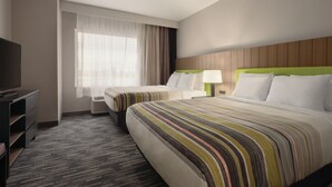 Une chambre d’hôtel avec deux lits, une télévision, un bureau et une fenêtre avec des rideaux.